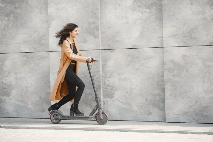 woman in brown coat riding a electric scooter